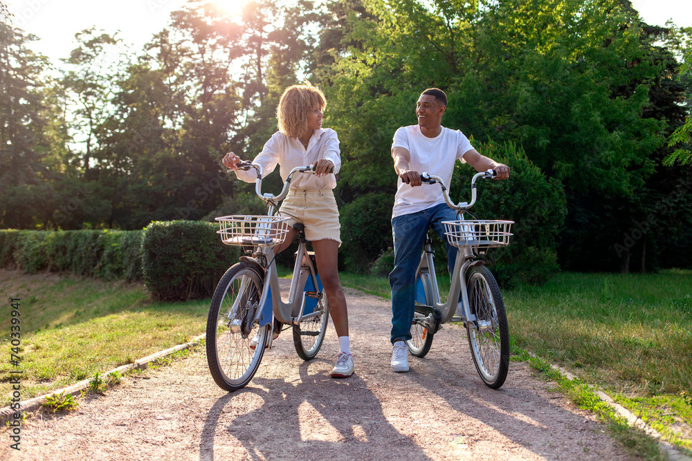 african-american couple rides bicycles in the park and talks, man and woman walk on eco-transport