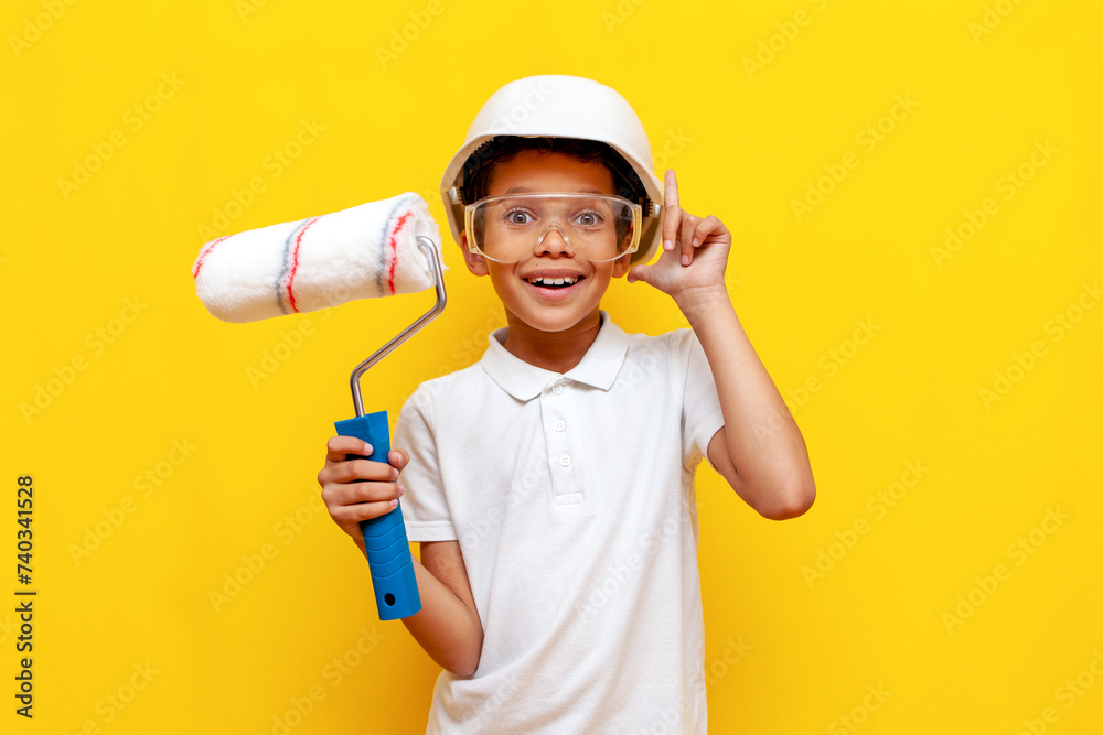 african american boy painter repairman in hard hat and safety glasses holds roller and points his finger up african american boy painter repairman in hard hat and safety glasses holds roller and points his finger up