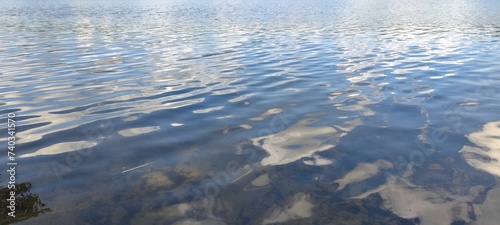 Transparent water of a forest lake. The wavy surface of the water in the rays of the setting sun. You can see the sandy bottom through the water. The sun's rays penetrate the water in curved lines.