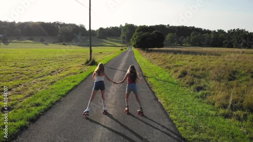 Two young women learning how to roller skate down a deserted country road in upstate NY. Childhood friends supporting each other. Filmed by drone. photo