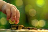 A child's finger is placing a gold coin on top. It's like saving money for a business. has green bokeh