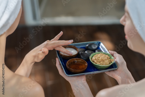 Portrait of two attractive women with beautiful holding the tray contained ingredients of homemade facial mask while using the facial mask. Focus on the ingredients. Blurring background. Tranquility.