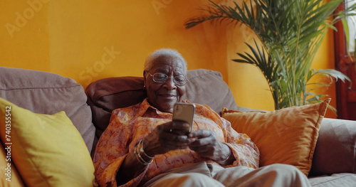 Sophisticated elderly black woman on her phone, relaxing in beautifully design interior with soft cool lighting, architecturally design home, posh home, with short focus portrait shot. Internet.
