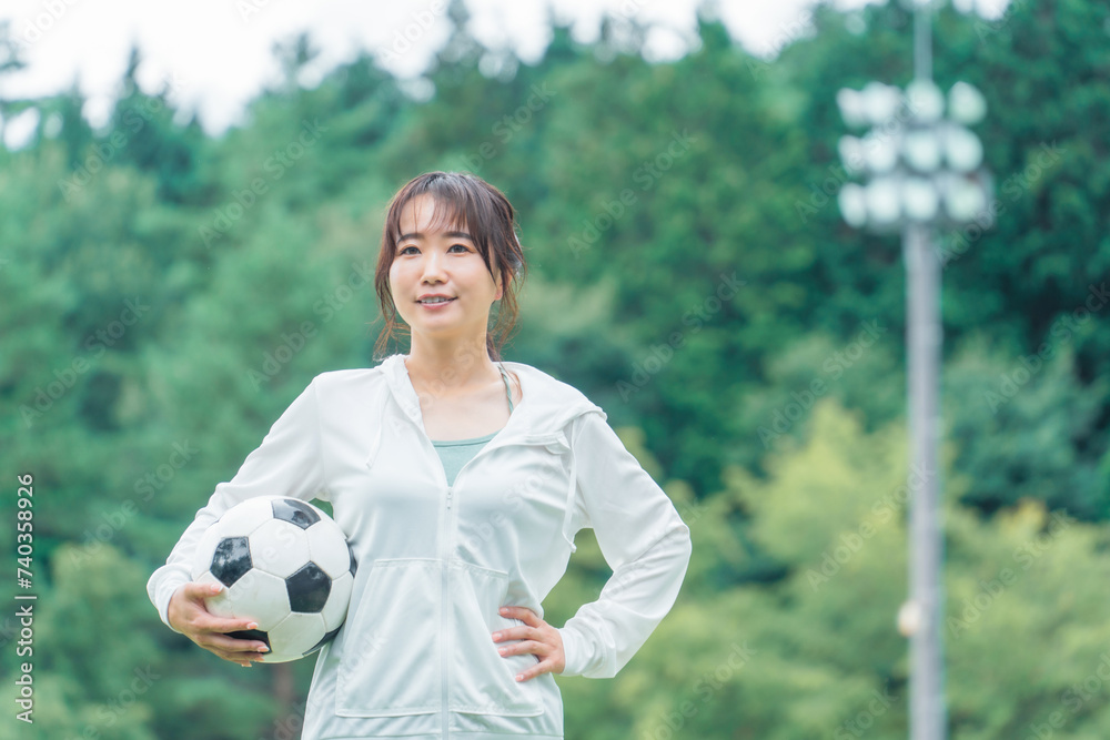Naklejka premium 運動場でサッカーボールを持つサッカーファン・サポーターの日本人女性 