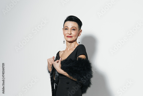 Elegant Asian Woman in a Stylish Black Dress and Fur Stole Posing Against White Wall