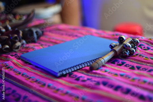 Notas Musicales. Libreta azul, junto a una sonaja de cascabeles sobre prenda rosa tipica mexicana.