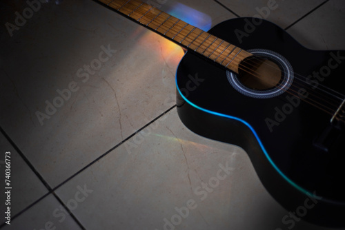 Música. Güitarra negra en el suelo, con rayo de luz multicolor callendo en el mastil. photo