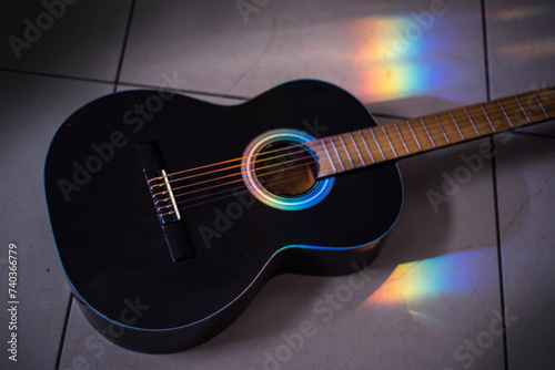 Música. Güitarra negra en el suelo, con rayo de luz multicolor callendo en la boca. photo