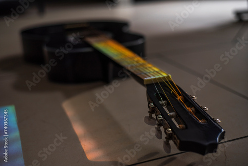 Música. Mastil, con clavijero de Güitarra negra acustica en el suelo en primer plano, con rayo multicolor cayendo sobre ellos.