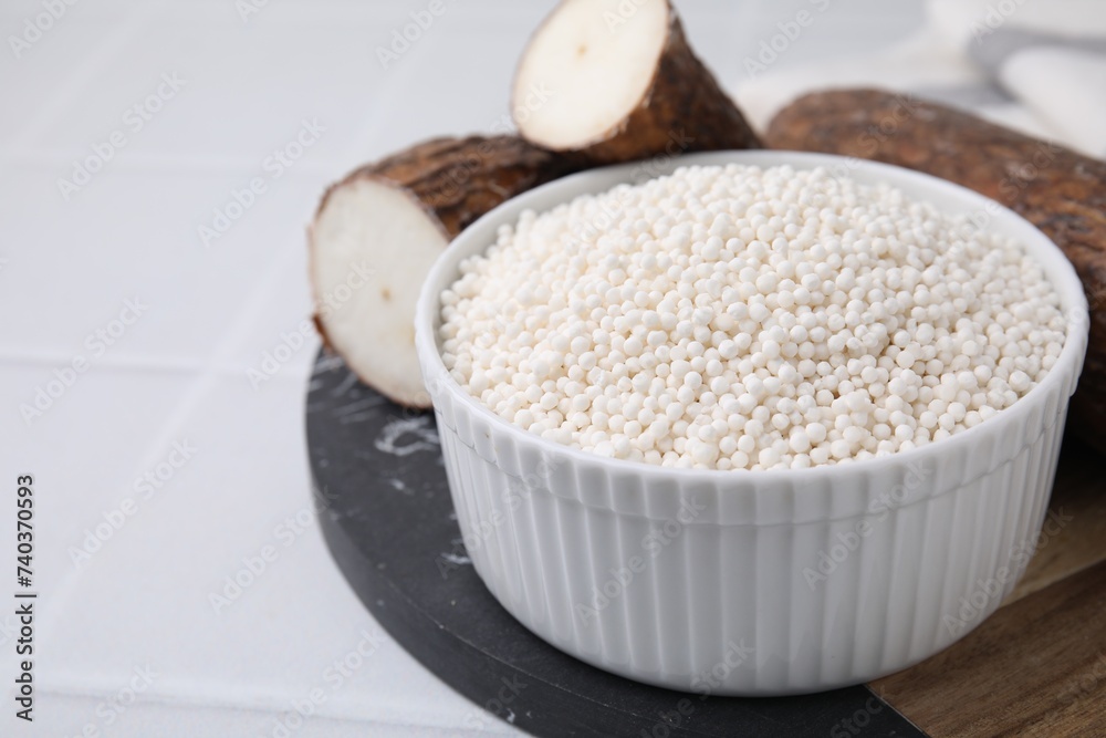 Tapioca pearls in bowl and cassava roots on white tiled table, closeup. Space for text Tapioca pearls in bowl and cassava roots on white tiled table, closeup. Space for text
