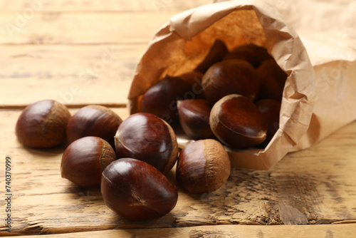 Sweet fresh edible chestnuts in paper bag on wooden table, closeup
