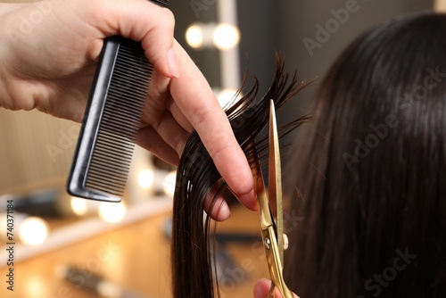 Hairdresser cutting client's hair with scissors in salon, closeup