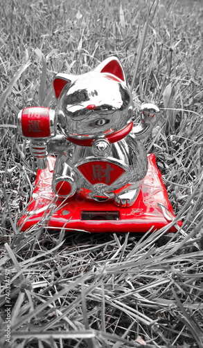 lucky cat solar cell. japanese doll energy ingot mean symbol of luck charm, with red figurine known as maneki neko happy on grass vertical black background.