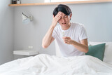 ベッドで体温計で熱を測る若いアジア人男性（発熱・風邪・コロナ・インフルエンザ・ワクチン・副作用）
