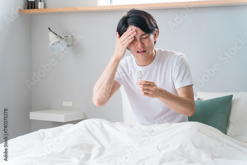 ベッドで体温計で熱を測る若いアジア人男性（発熱・風邪・コロナ・インフルエンザ・ワクチン・副作用）
 photo