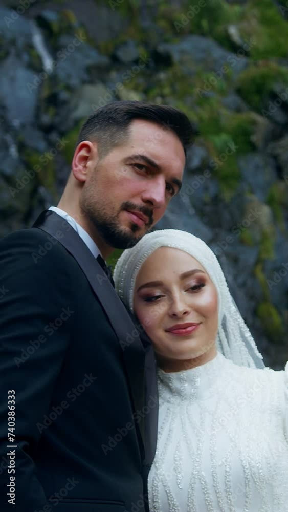 Vertical video. Young happy bride and groom standing in front of a waterfall smiling and posing outdoors
Vertical video. Young happy bride and groom standing in front of a waterfall smiling and posing outdoors