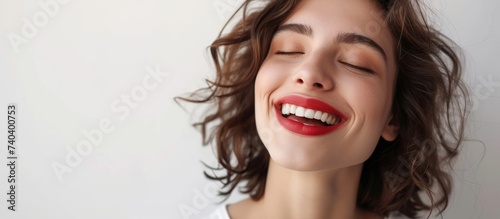 A happy woman wearing red lipstick is flashing a closed-eye smile  showcasing her lips  chin  jawline  and neck in her joyful gesture.