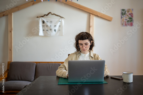 Serious freelance girl in glasses working at home with laptop searching information for project. Focused young woman engrossed in job on computer harmonious blend of technology gadget and domesticity photo