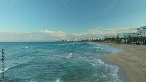 Wallpaper Mural Aerial - panoramic view of a bustling beachfront in Cyprus, with gentle waves lapping the sandy shore. The skyline is dotted with a mix of modern buildings and greenery under a partially cloudy sky. Torontodigital.ca