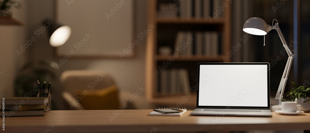 A modern, cozy home office at night with a white-screen laptop computer mockup on the table.