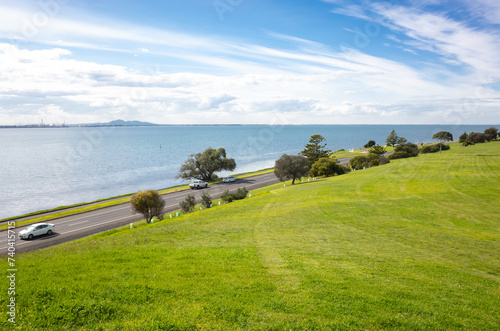 Background texture of large grass lawn with a beautiful harbour view and cars on a scenic road. A public park with a sea view in Geelong, VIC Australia. Copy space for your design.
