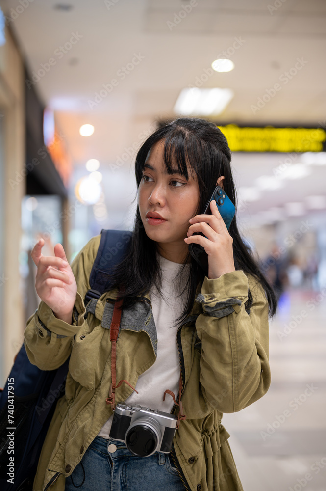 Fototapeta premium A young Asian female traveler is talking on the phone with someone while walking in the airport.
