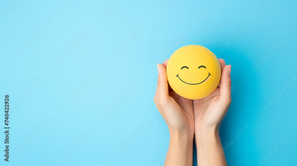 Hands Holding a Smiley Face Ball Against a Bright Blue Background, Concept of Happiness and Positivity