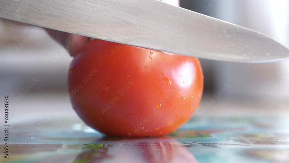 sharp chef's knife slicing tomato on cutting board close up in slow motion