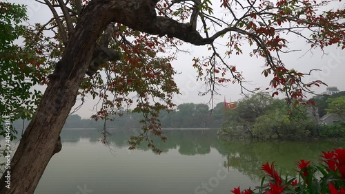 From the shoreline of Hoan Kiem lake looking down from the red leaves to the red flowers and Cau The Huc bridge. photo