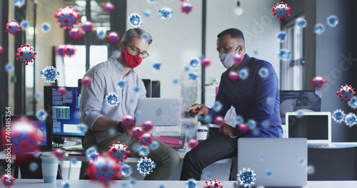 Image of virus cells floating over diverse businessmen with face masks at meeting