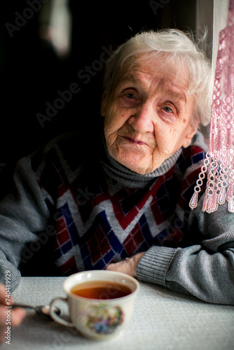 An old woman drinking tea in the kitchen.