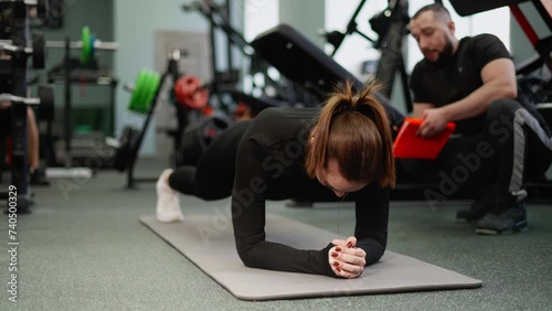A female athlete performs a plank exercise. The coach encourages and monitors the correct posture. photo