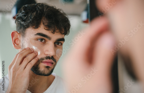 Man looking in mirror, applying eye patches in bathroom. Spending quality time at home alone, skincare, domestic life and lifestyle concept. photo
