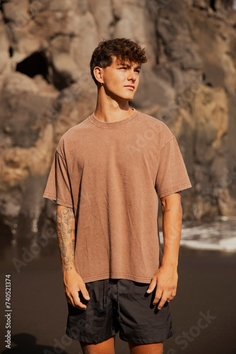 Portrait of handsome tattooed guy with brown hair posing on the beach