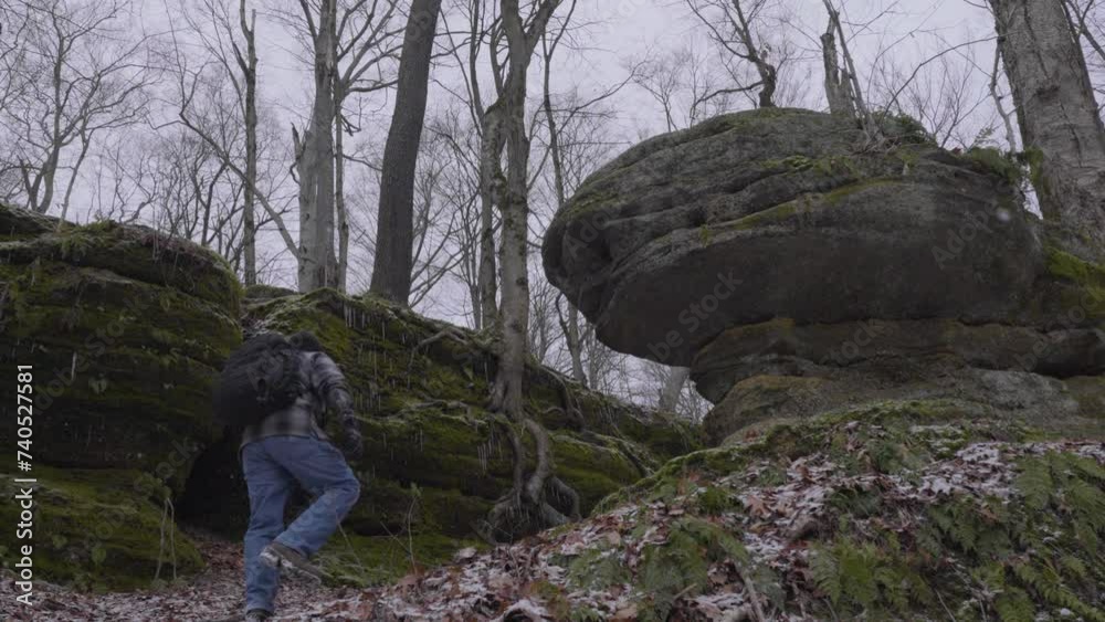a lone hiker walks up the mountainside with barren trees and moss covered cliffs and ledges a lone hiker walks up the mountainside with barren trees and moss covered cliffs and ledges