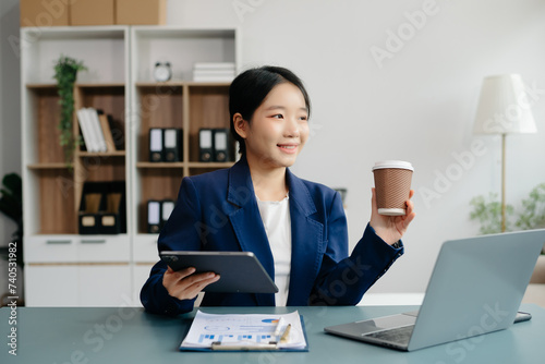 Confident Asian woman with a smile standing holding notepad and tablet at the office.