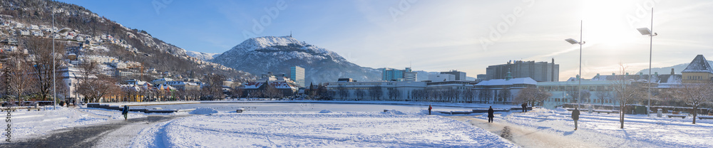 Wide panorama of Lille Lungegårdsvannet or lake in the central bergen in winter, covered with snow and ice. Visible cityscape of Bergen in Sunny weather.