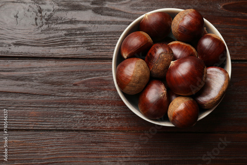 Sweet fresh edible chestnuts in bowl on wooden table, top view. Space for text