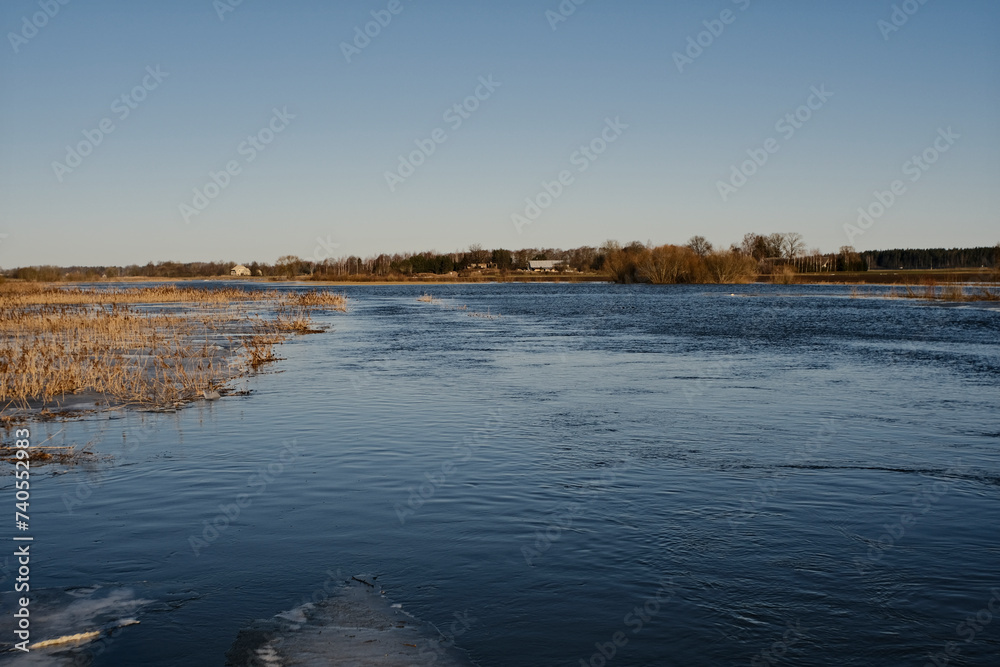 Overflown river Svitene in Latvia, Zemgale. Floods in sunny early spring day. Blue clear sky. Water on meadows and fields.