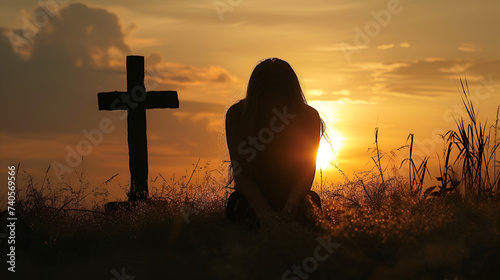 Silhouette of a woman sitting on the grass praying in front of a cross at sunset. generative ai