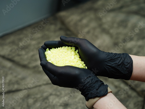 Granulated gold wax for depilation. Depilation master in black protective gloves holds granular yellow depilatory wax