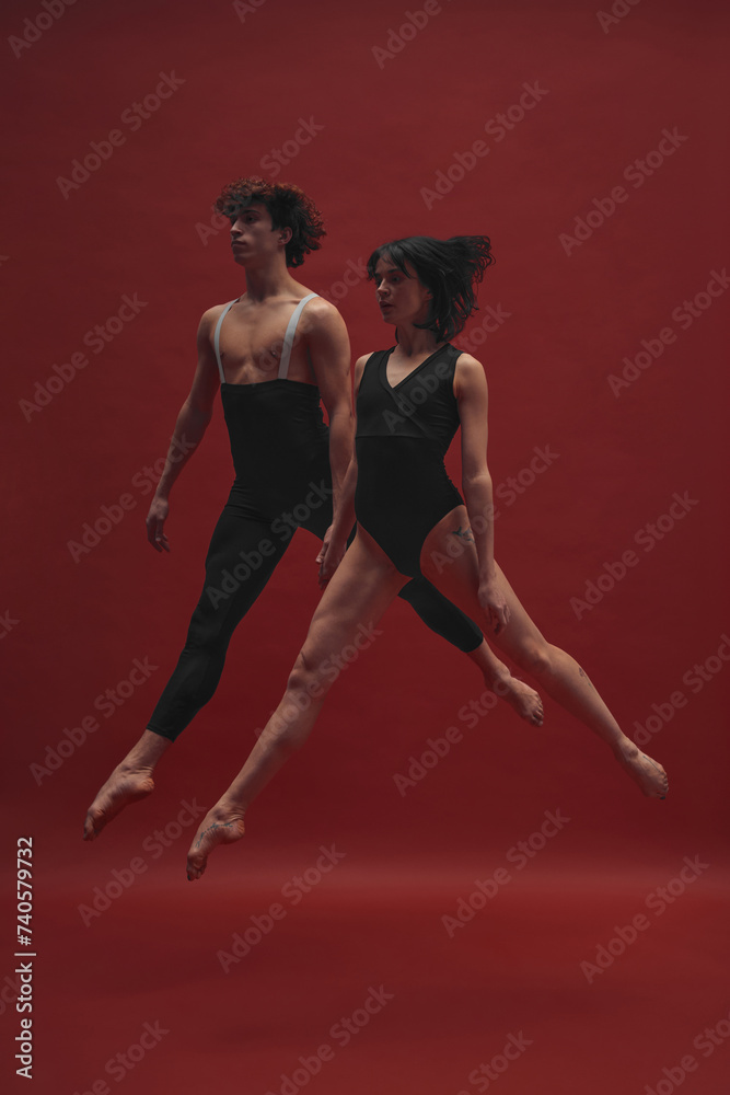 Young man and woman, ballet dancers in black cloths dancing, performing against red background. Concept of classic art, aesthetics, emotions, ballet dance, talent, beauty Young man and woman, ballet dancers in black cloths dancing, performing against red background. Concept of classic art, aesthetics, emotions, ballet dance, talent, beauty