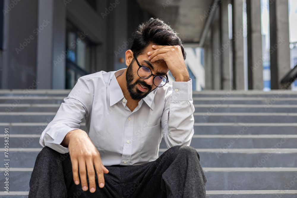 A stressed businessman in despair sits on outdoor steps, expressing worry and frustration, embodying work-related stress. A stressed businessman in despair sits on outdoor steps, expressing worry and frustration, embodying work-related stress.
