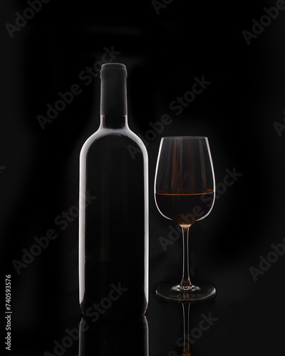 Isolated bottle of red wine and red glass of wine on black background without label