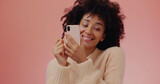 Beautiful young black woman texting on cell phone and giggling at flirty text, pink background