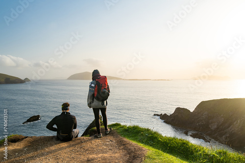 Couple of tourists at Dunquin or Dun Chaoin pier, Ireland's Sheep Highway. Narrow pathway winding down to the pier, ocean coastline, cliffs. Slea Head Drive, Wild Atlantic Way. photo