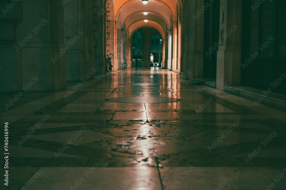 Fototapeta premium Under the porticoes of a historic building in the city center at night. Old building in the city center with lights. Reflecting stone floor. Udine city center old bulding in the night. Historical city