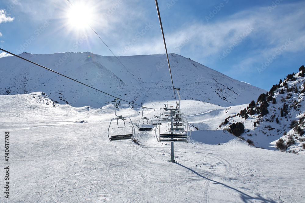 Chunkurchak ski resort in Kyrgyzstan. Empty ski lift seats. Mountain slope at sunny winter day, blue sky. Active recreation skiing and snowboarding. Support pillar, Cable car ride.
