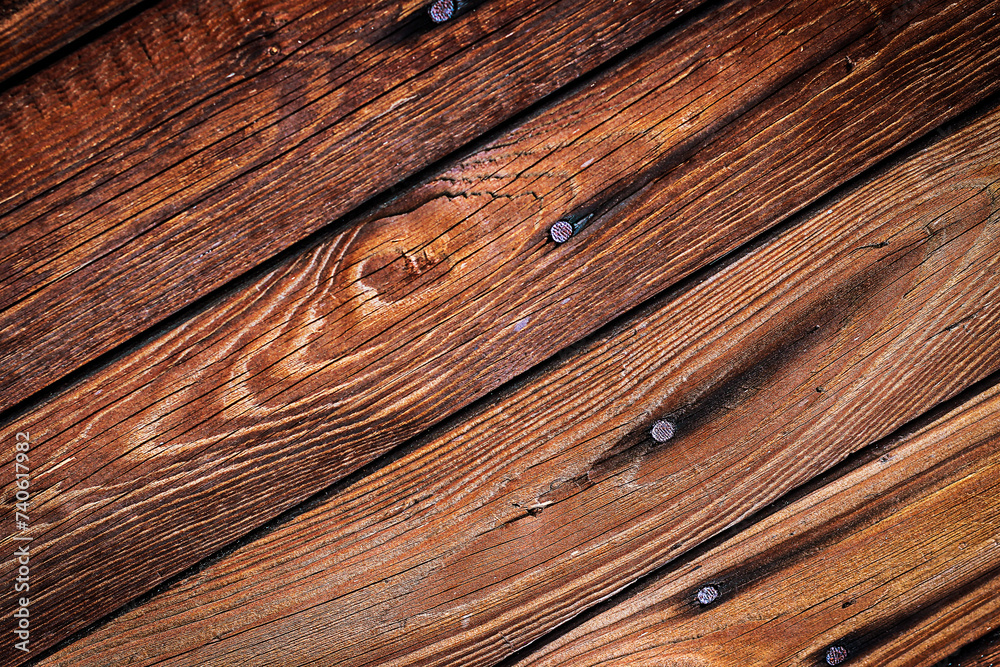 Naklejka premium Brązowe chropowate drewniane deski przybite gwoździami z widocznymi słojami i sękami ułożone ukośnie – tło, tekstura