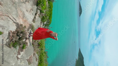 Woman on red dress standing on the coast with crystalline turquoise sea in Arraial do Cabo, Rio de janeiro, Brazil. Aerial drone vertical view. photo